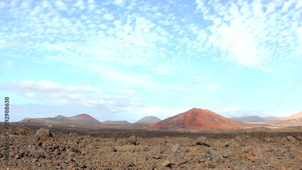 Red mountain in volcanic landscape with cotton clouds over blue sky background in Lanzarote, Canary Islands. Natural scenery, empty tourist destination concepts Red mountain in volcanic landscape with cotton clouds over blue sky background in Lanzarote, Canary Islands. Natural scenery, empty tourist destination concepts