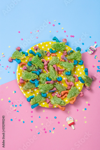 Green  pink and blue chewing marmalade  candy frogs on yellow plate on a pink and blue background. Flat lay  top view.