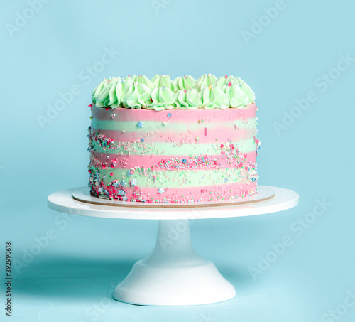 Classic light pink and blue stripes Birthday sweet cake with colorful sprinkles over a popular light turquoise mint on white stand background 
