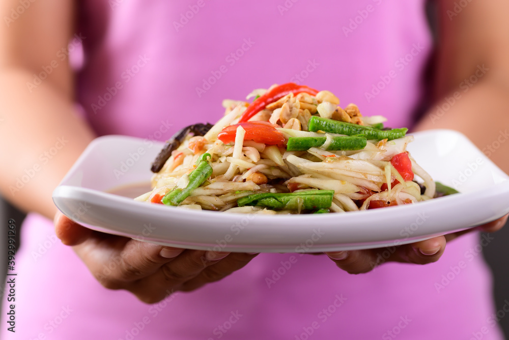 Thai food (Som Tum), Spicy green papaya salad on plate holding by hand Thai food (Som Tum), Spicy green papaya salad on plate holding by hand
