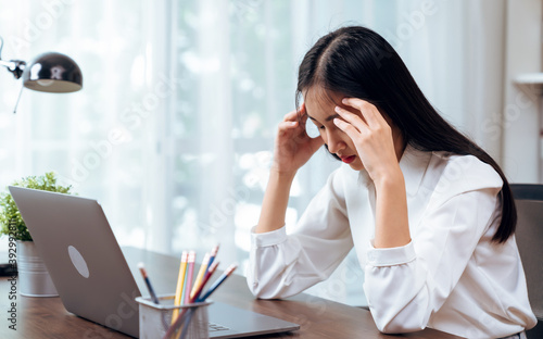 Asian business woman suffers from headache from working with computers for a long time.. © Chayjitti