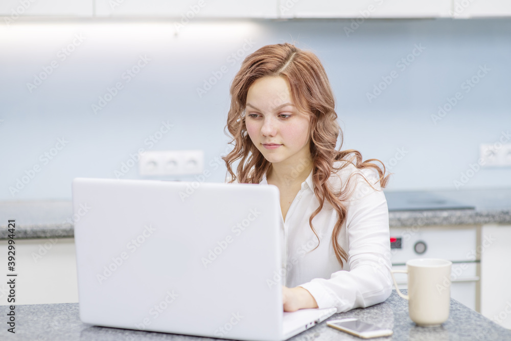 A girl is sitting in her kitchen at a notebook with a phone next to her. Online shopping concept A girl is sitting in her kitchen at a notebook with a phone next to her. Online shopping concept