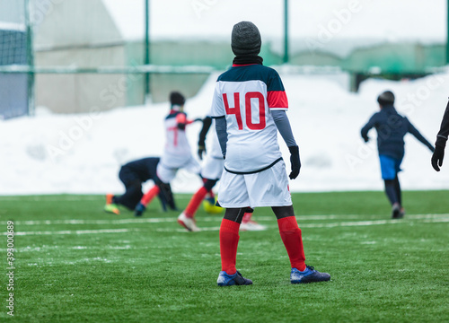 Boys in white sportswear running on soccer field with snow on background. Young footballers dribble and kick football ball in game. Training, active lifestyle, sport, children winter activity © Natali