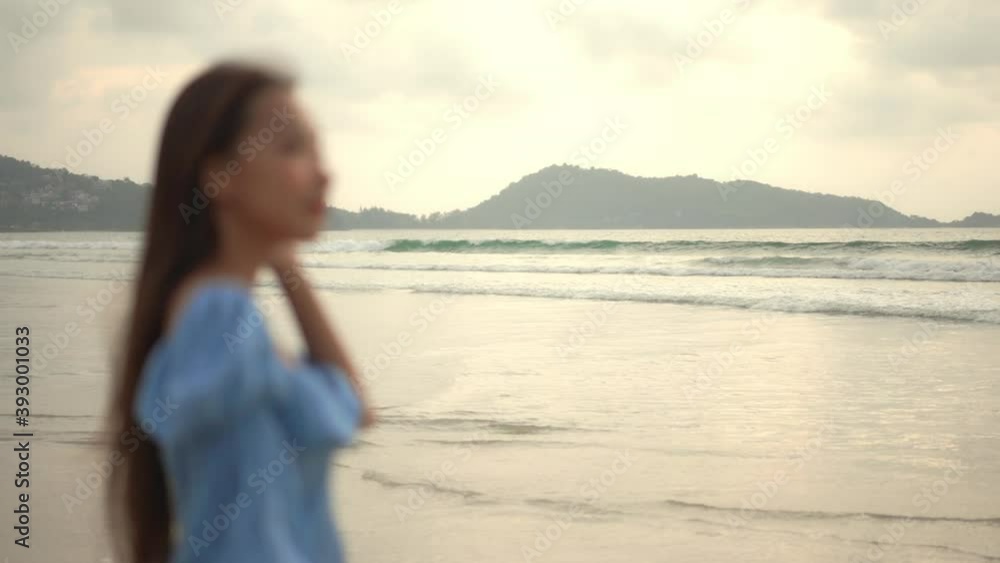 Rack focus from the background beach and waves rolling on to a pretty young woman in the foreground of the frame. Rack focus from the background beach and waves rolling on to a pretty young woman in the foreground of the frame.