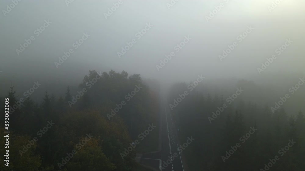 Aerial jib down lower view of straight empty road through foggy forest on gray day Aerial jib down lower view of straight empty road through foggy forest on gray day