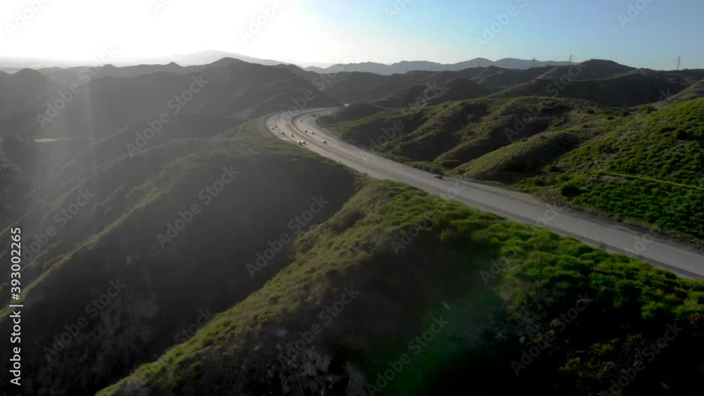 Winding highway bends through empty rolling hills covered in green grass as seen from above aerial as cars and trucks travel and ship. Winding highway bends through empty rolling hills covered in green grass as seen from above aerial as cars and trucks travel and ship.