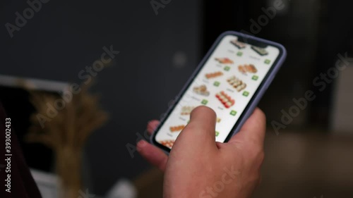 A man at home, in the living room, buys sushi from an online store for a courier to deliver it. A man orders food at home in an online store using a smartphone. A man chooses dinner at a restaurant