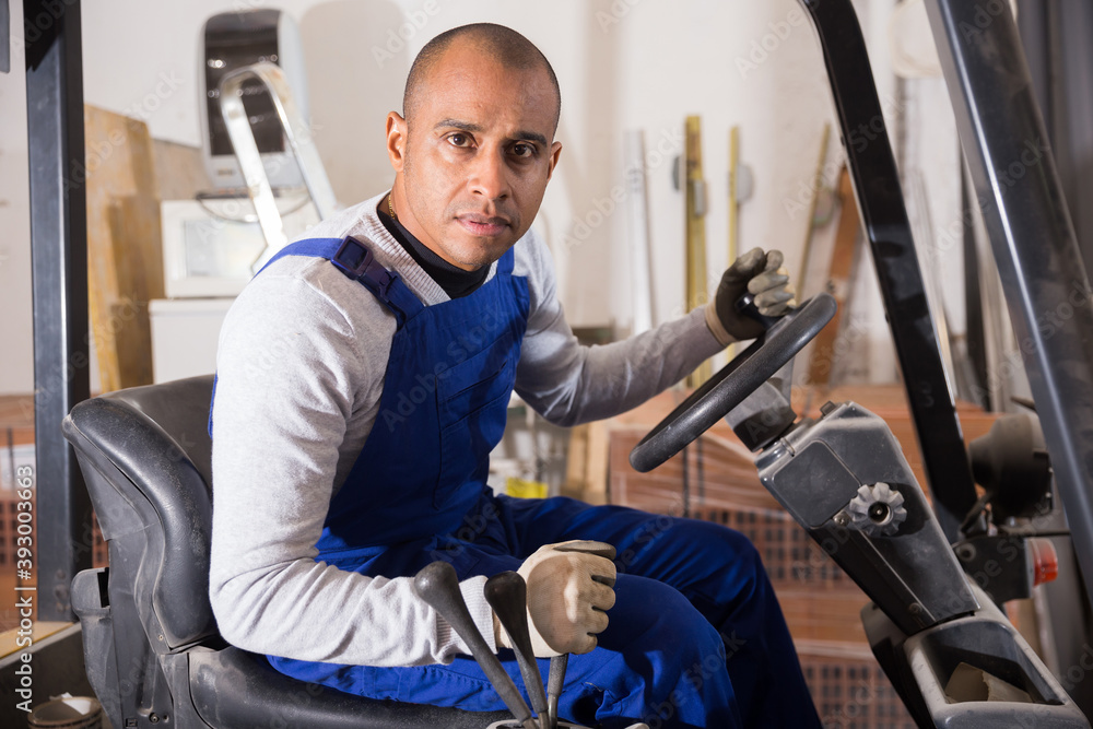 Obraz premium Skilled hispanic worker of building materials warehouse working on forklift truck..