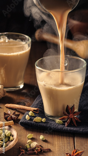 Masala tea with spices is poured into glass mugs on a wooden table.