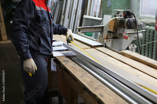 A photo of a worker measures a window sill with a tape measure for cutting on a miter saw. Industrial concept.