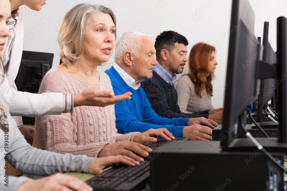 Portrait of mature woman attentively listening young female coach during computer classes