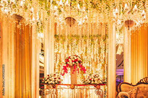 table of three decorated bouquets of white and pinks flowers with strings of flowers hanging and light of three bright warm chandeliers glowing the decoration at an Indian wedding party stage. photo