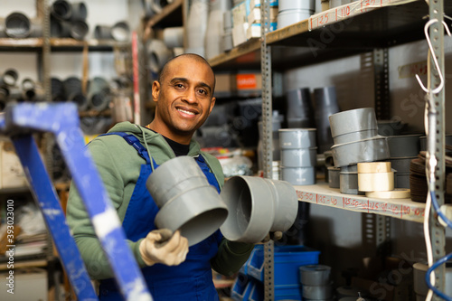 Salesman in overalls with plumbing fittings at a hardware store warehouse