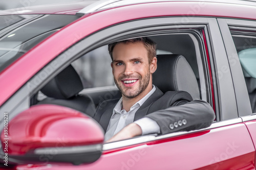 Smiling young male drivig red car, elbow out of window