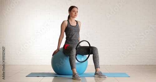 Sporty young woman doing pilates with fitball and isotonic ring in gym