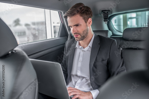 Brown-haired male sitting at backseat of car, working on laptop © zinkevych