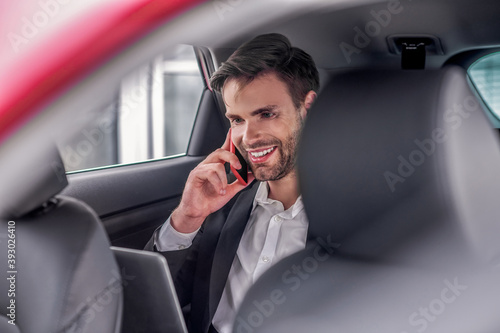 Smiling male sitting at backseat of car with laptop, talking on phone © zinkevych