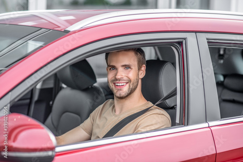 Smiling bearded young male driving red car