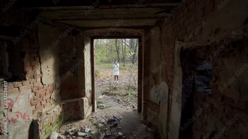Looking at young woman in the park through the window frame of a destroyed house woman on cold autumn day with trees covered in yellow leaves Looking at young woman in the park through the window frame of a destroyed house woman on cold autumn day with trees covered in yellow leaves