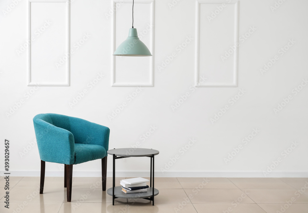 Stylish armchair with table and books near light wall in room Stylish armchair with table and books near light wall in room