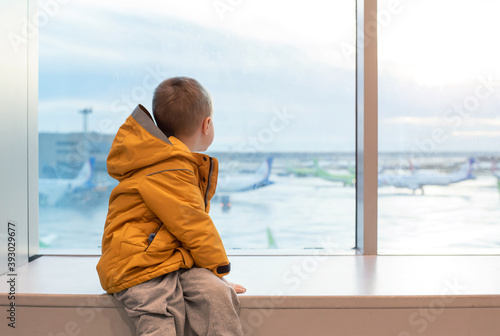 A boy in a yellow jacket at the airport at the big window.