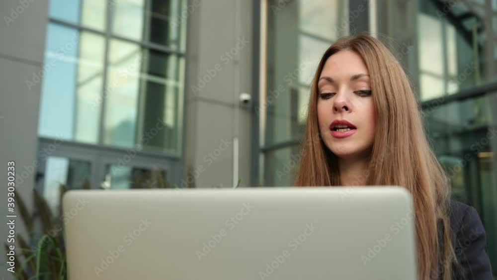 Remote conference with a laptop sitting on bench in the street. Happy brunette woman having video call. Young caucasian female conversation person outside computer. Close up Remote conference with a laptop sitting on bench in the street. Happy brunette woman having video call. Young caucasian female conversation person outside computer. Close up
