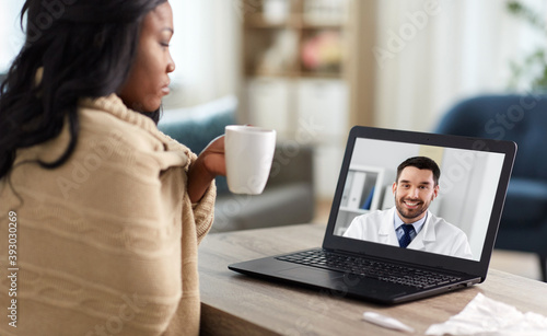 healthcare, technology and people concept - african american sick woman in blanket having video call or online consultation with smiling doctor on laptop computer at home