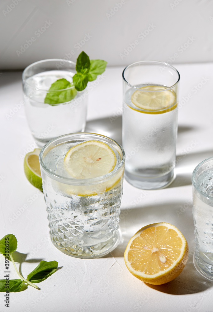 drink, detox and diet concept - glasses with fruit water or lemonade, lemons, limes and peppermint on white table drink, detox and diet concept - glasses with fruit water or lemonade, lemons, limes and peppermint on white table