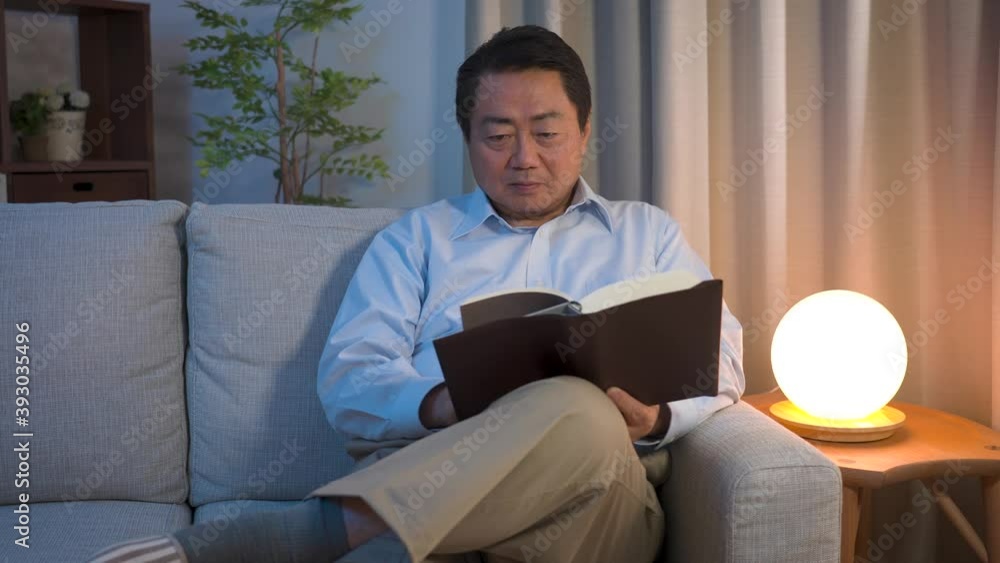 ソファーで本を読んでいる中年男性 ソファーで本を読んでいる中年男性