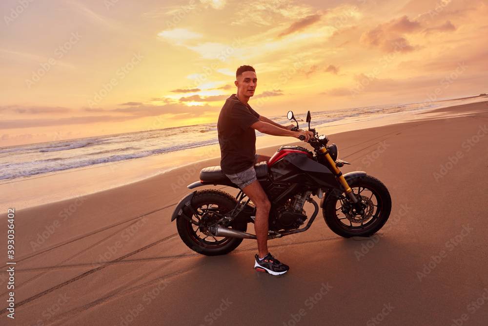 Man And Motorcycle On Ocean Beach At Beautiful Tropical Sunset. Handsome Biker On Motorbike On Sandy Coast In Bali, Indonesia. Man And Motorcycle On Ocean Beach At Beautiful Tropical Sunset. Handsome Biker On Motorbike On Sandy Coast In Bali, Indonesia.