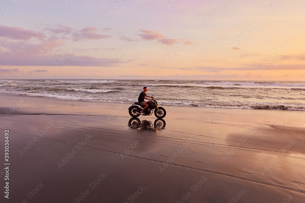 Fototapeta premium Man And Motorcycle On Ocean Beach At Beautiful Tropical Sunset. Biker’s Silhouette On Motorbike On Sandy Coast Near Sea In Bali, Indonesia.