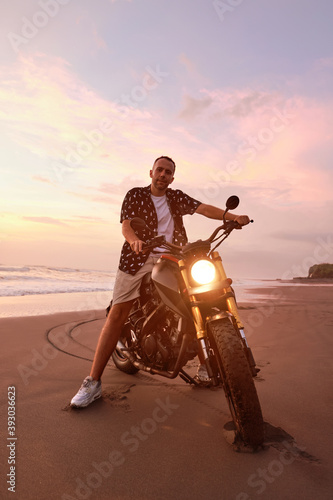 Man’s On Motorcycle Portrait On Ocean Beach At Beautiful Tropical Sunset. Front View Of Handsome Biker On Motorbike On Sandy Coast In Bali, Indonesia.