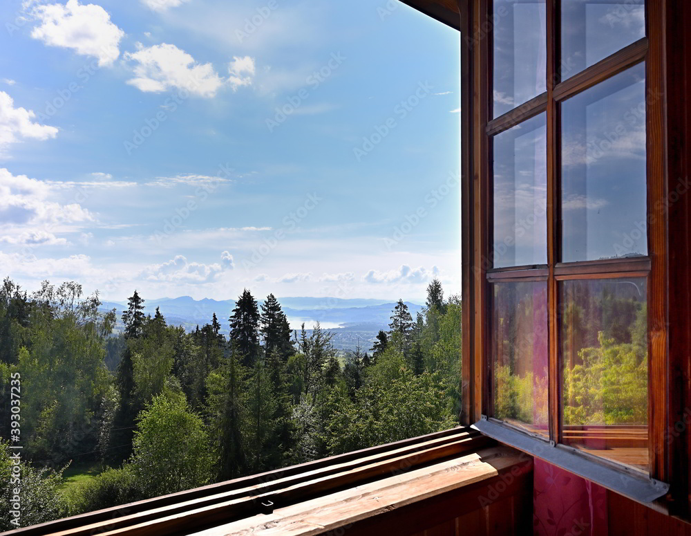 Beautiful view on green trees forest, blue sky and mountains through a wooden window frame of an old house cottage on a slope of a hill in southern Poland Beautiful view on green trees forest, blue sky and mountains through a wooden window frame of an old house cottage on a slope of a hill in southern Poland