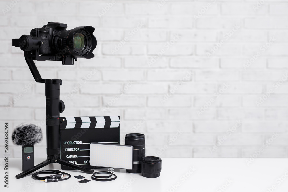 videography concept - modern dslr camera on 3-axis gimbal stabilizer,  lenses, microphone, led light, clapper board and other videography  equipment over white brick wall background Stock Photo | Adobe Stock