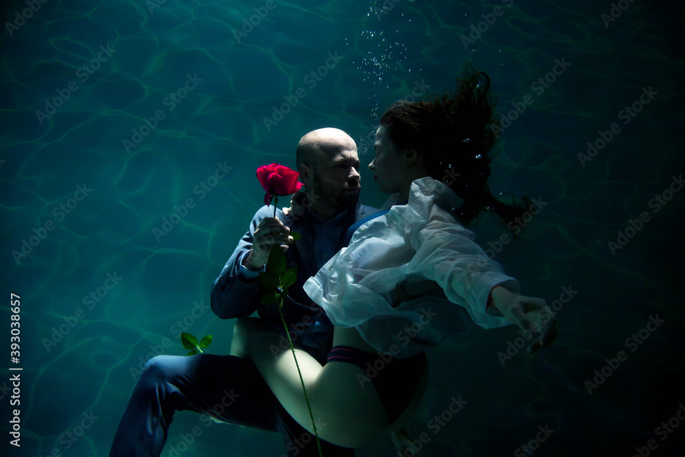 Young businessman embraces his woman, gives rose, kisses beloved, underwater. Emotional happy couple in pond. Concept romantic date, surprise and commitment to development of relations. Copy space