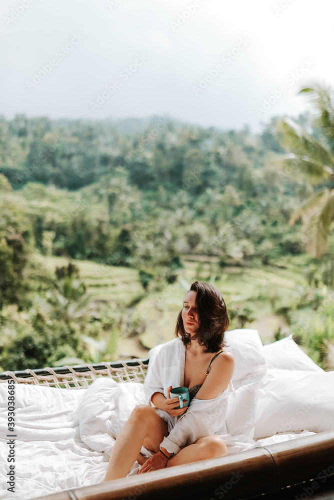 Young travel blogger and influencer girl relaxing in a bamboo house hotel in Bali surrounded by rice terraces and palm trees