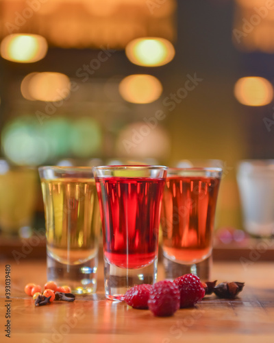 Tincture alcoholic in small shot glasses. Natural fruit alcohol drinks, shots served on a wooden table.