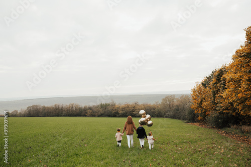Mother  little daughters and son with golden balloons on the field in autumn day. Copy space.