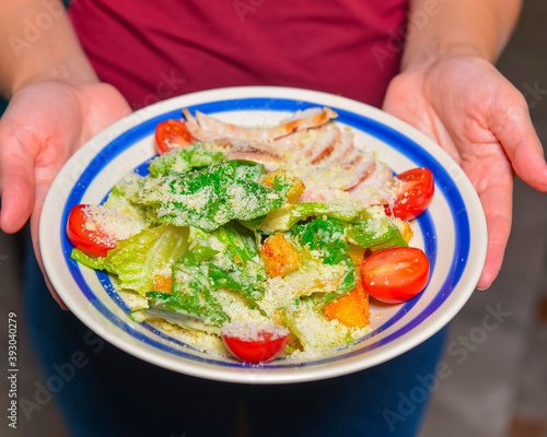 Fototapeta Naklejka Na Ścianę i Meble -  Bowl of Caesar Salad. Waiter in restaurant holds a plate of Italian caesar salad. Traditional Italian cuisine.