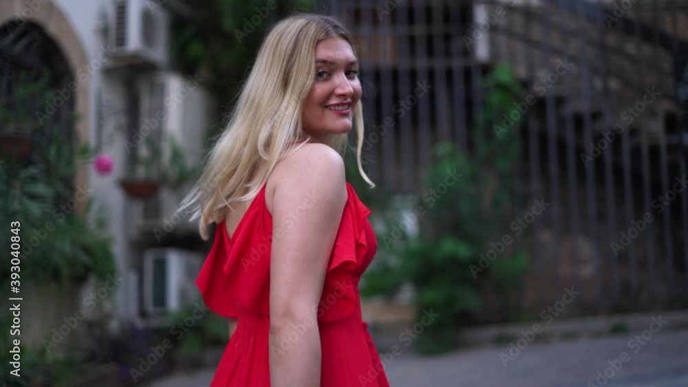 Charming smiling woman with loose blonde hair wearing trendy long bright red dress walks swirling against defocused streets of calm ancient town slow motion. Charming smiling woman with loose blonde hair wearing trendy long bright red dress walks swirling against defocused streets of calm ancient town slow motion.