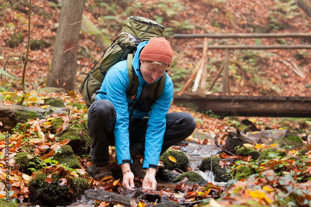 Backpacker scooping water from a mountain creek in autumn Backpacker scooping water from a mountain creek in autumn