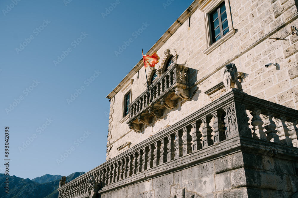 Red flag of Montenegro on a building with a large balcony among the mountains against a blue sky.