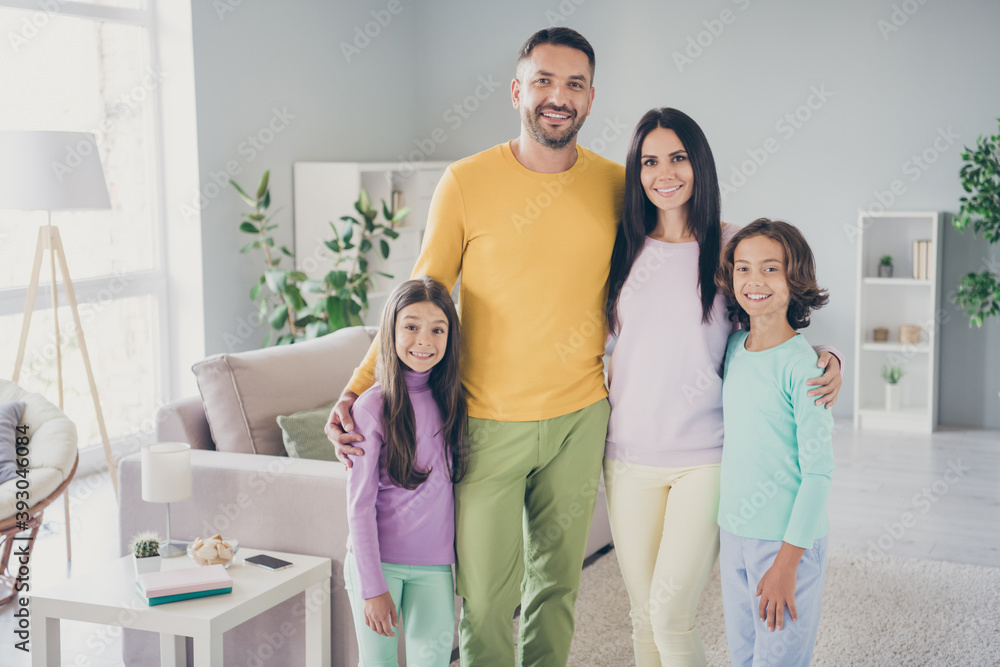 Fototapeta premium Photo of full family four members meeting two small children cuddle look camera wear colorful pullover pants in living room indoors