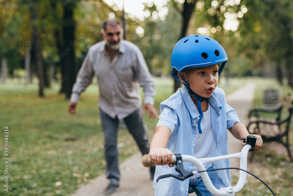 boy teaching to ride bike with his grandfather in public park boy teaching to ride bike with his grandfather in public park