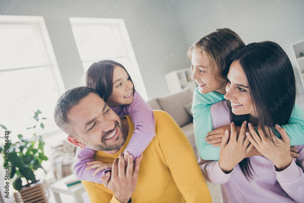 Photo of big family four people foster parents hold piggy back adopted kids wear colorful pullover in living room indoors Photo of big family four people foster parents hold piggy back adopted kids wear colorful pullover in living room indoors