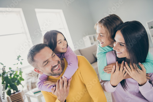Photo of big family four people foster parents hold piggy back adopted kids wear colorful pullover in living room indoors