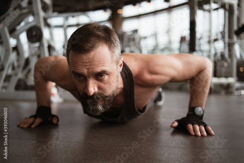 Fototapeta Naklejka Na Ścianę i Meble -  Training in gym, Handsome man with a mustache, do muscle building exercises using dumbbells, focusing on lifting and sit-ups in a fitness sport