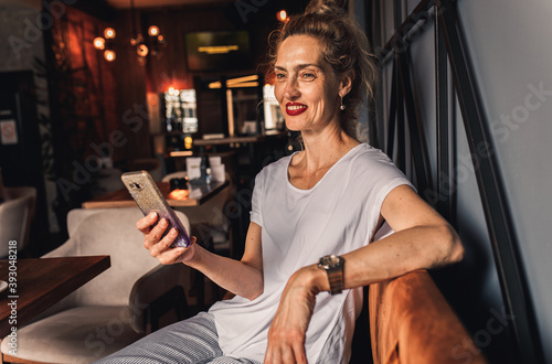 Smiling senior woman sitting in coffee shop drinking coffee and using smartphone.