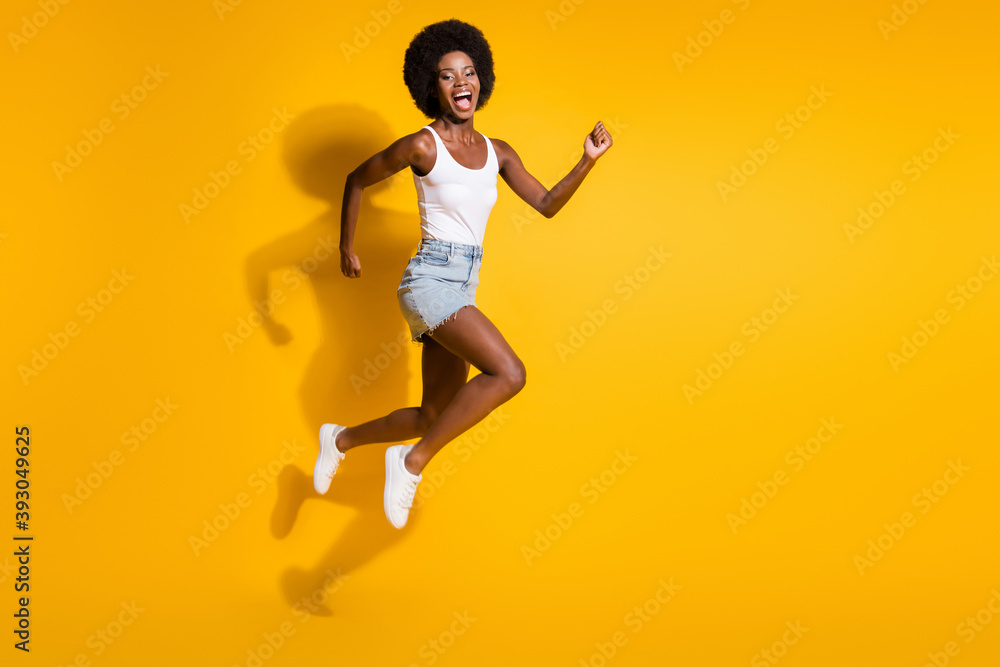 Full length body size view of active energetic cheerful wavy-haired girl jumping running fast isolated over bright yellow color background Full length body size view of active energetic cheerful wavy-haired girl jumping running fast isolated over bright yellow color background