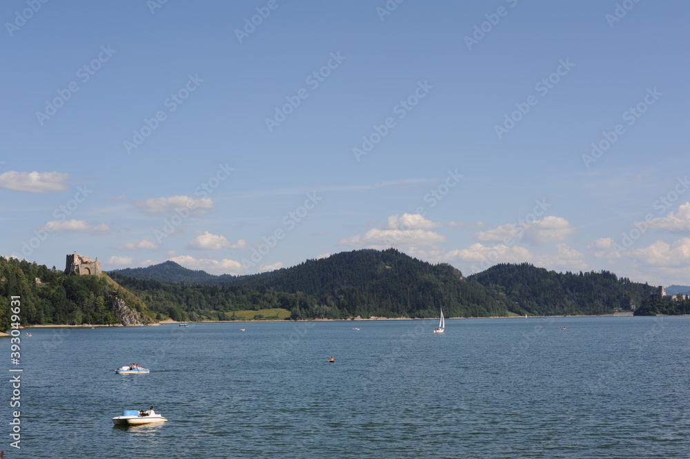Blue waters of Czorsztyn dam lake with yacht and green hills and mountains and blue sky with clouds in summer in southern Poland